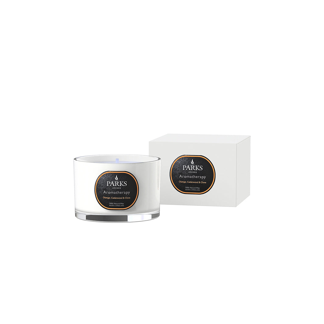 A Parks brand aromatherapy candle with orange, cedar, and clove scents, presented in a white glass jar with a label and a matching box.