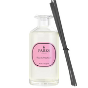 A clear glass diffuser bottle with a pink label, titled 'Rose & Patchouli', and black reeds attached to the side.