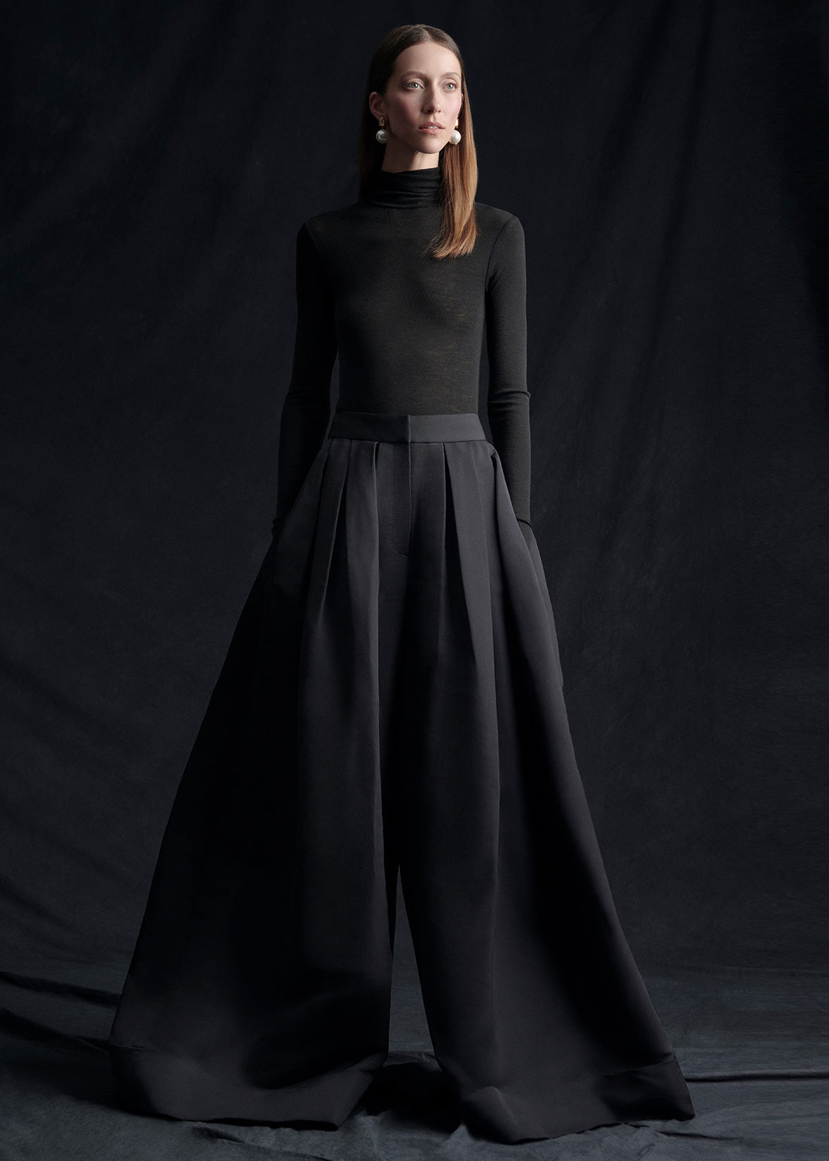 A model wearing silk faille wide leg pants and a black turtleneck.