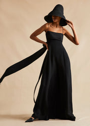 A campaign image of a model earing a black silk jumpsuit. 