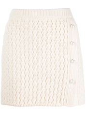 A flat-lay image of a knit ivory mini skirt with pearl buttons down the side.